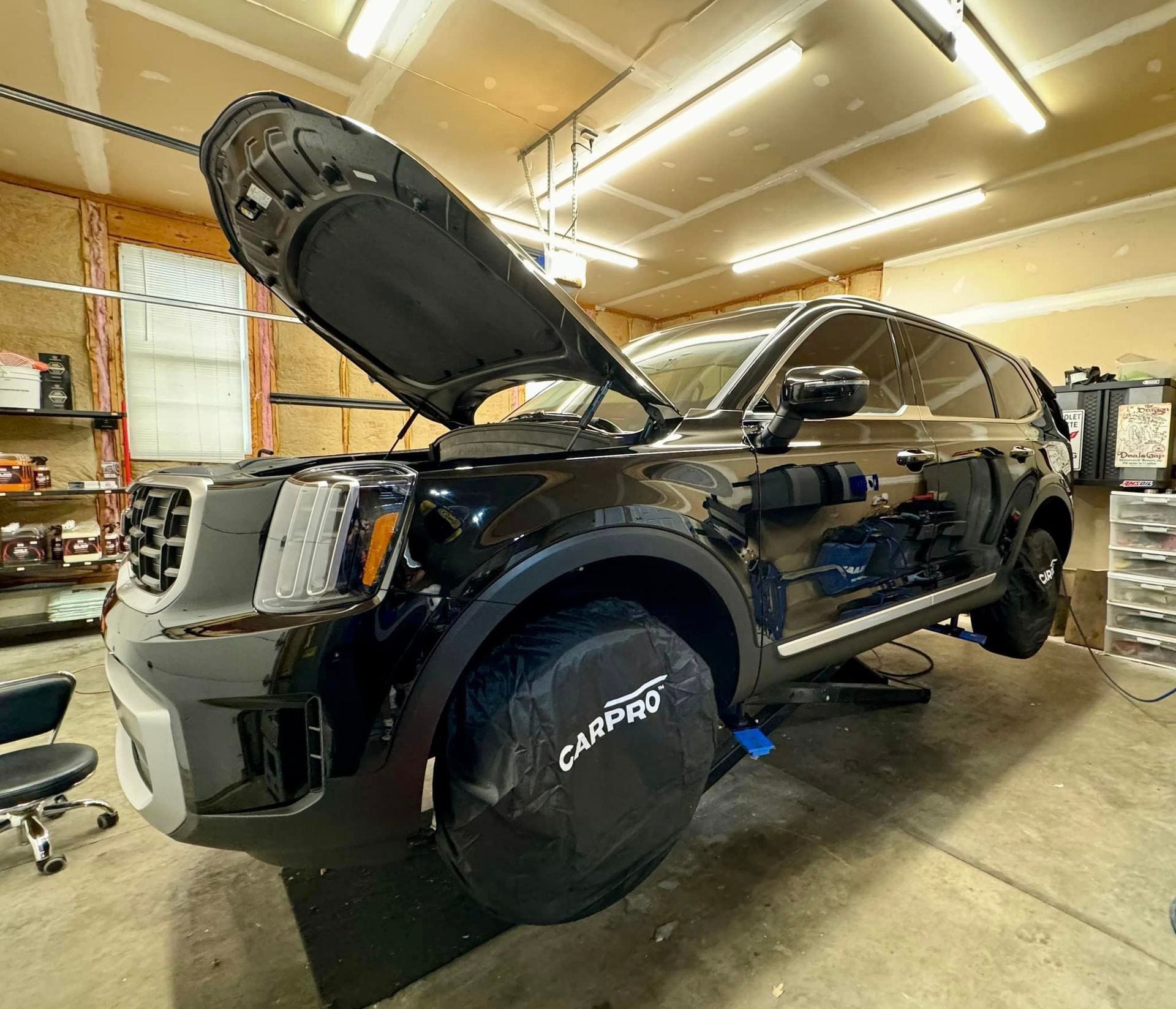 A black SUV with the hood up is sitting in a garage in EG Automotive detailing facility