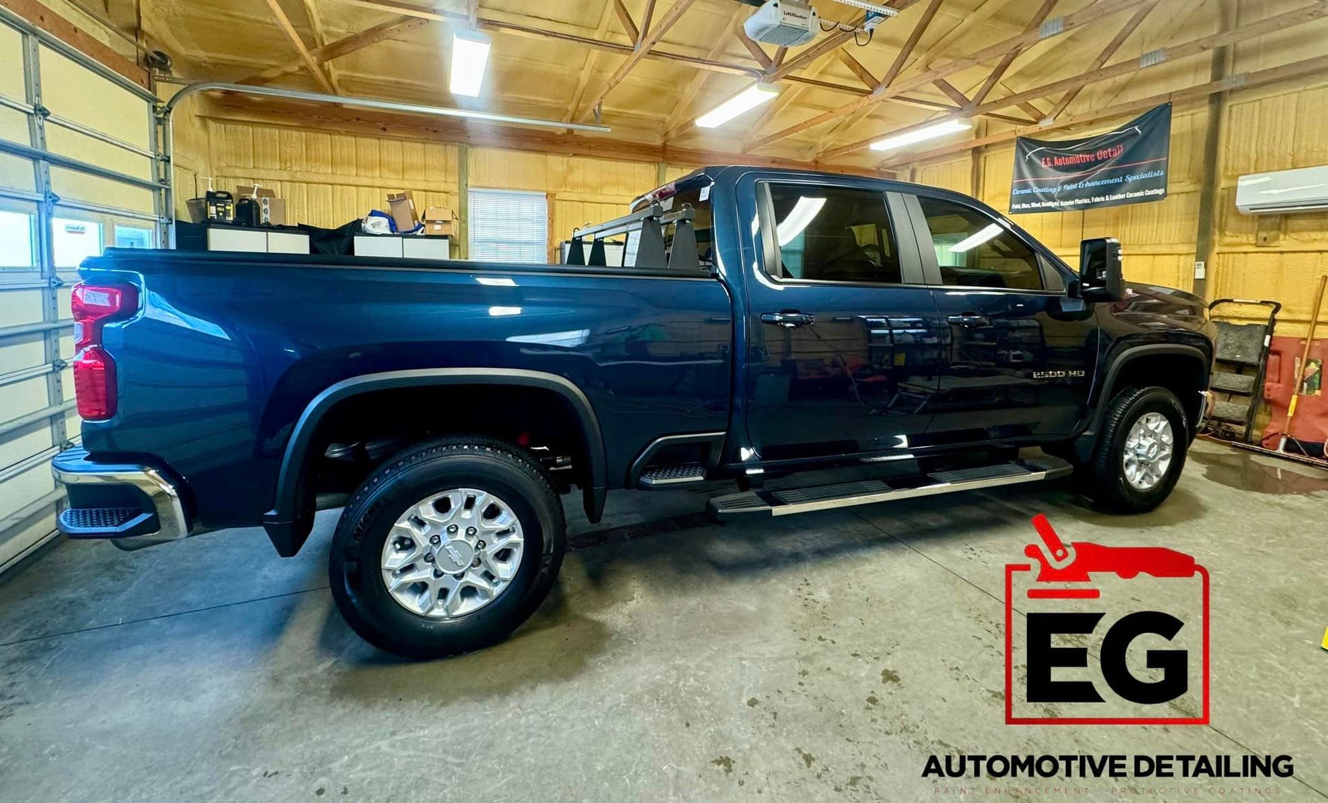 A blue truck is parked in a garage next to a garage door in EG Automotive detailing facility