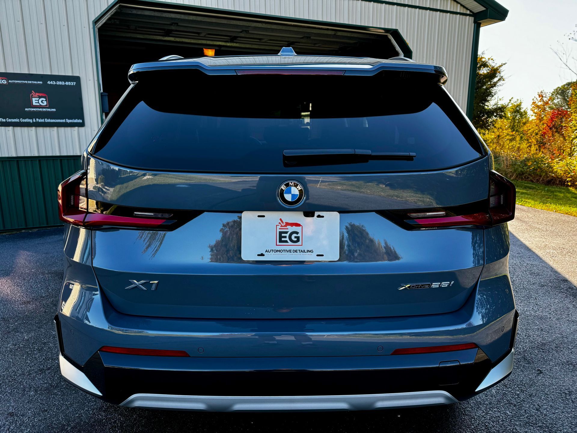 A bmw x1 is parked in front of a garage in EG Automotive detailing facility