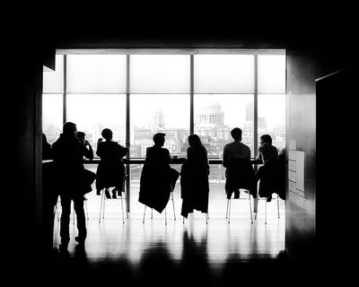 A group of people are sitting at tables in front of a large window.