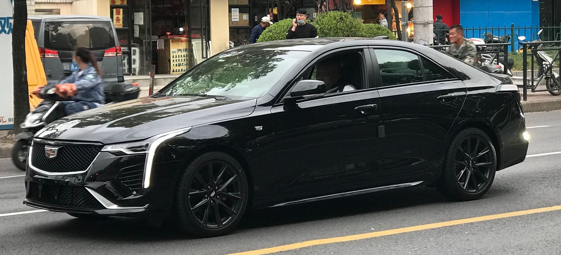 A black car is driving down a city street.