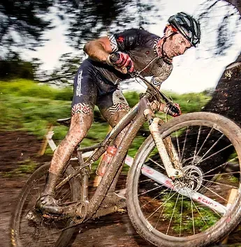 Mountain biker covered in mud, riding through a muddy trail.