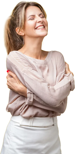 A person in a pale pink long-sleeve shirt and white skirt hugs themselves with a joyful, eyes-closed expression.