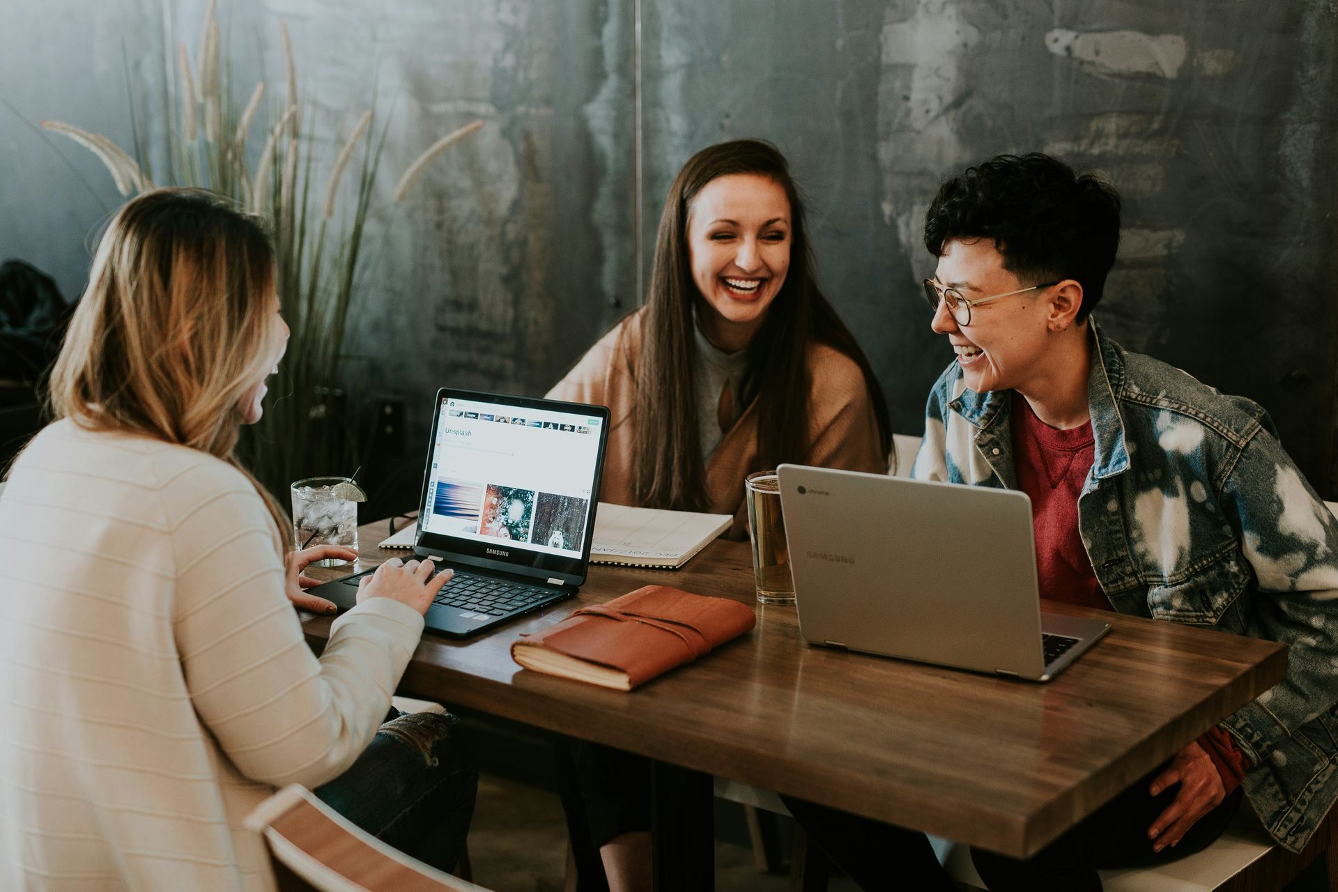 Three coworkers laughing around table during casual, joyful office meeting.