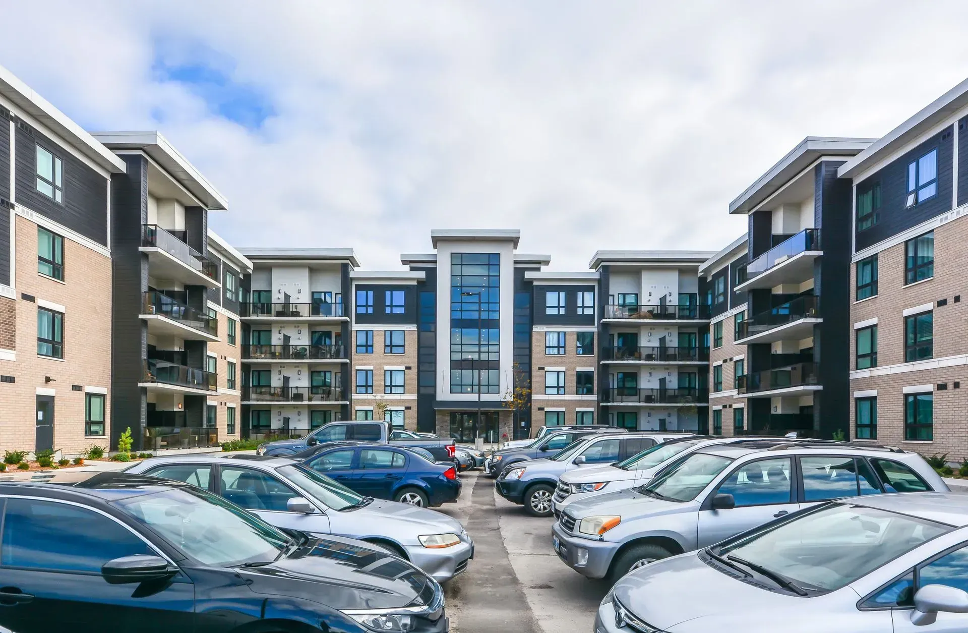 A parking lot filled with cars in front of a large apartment building.