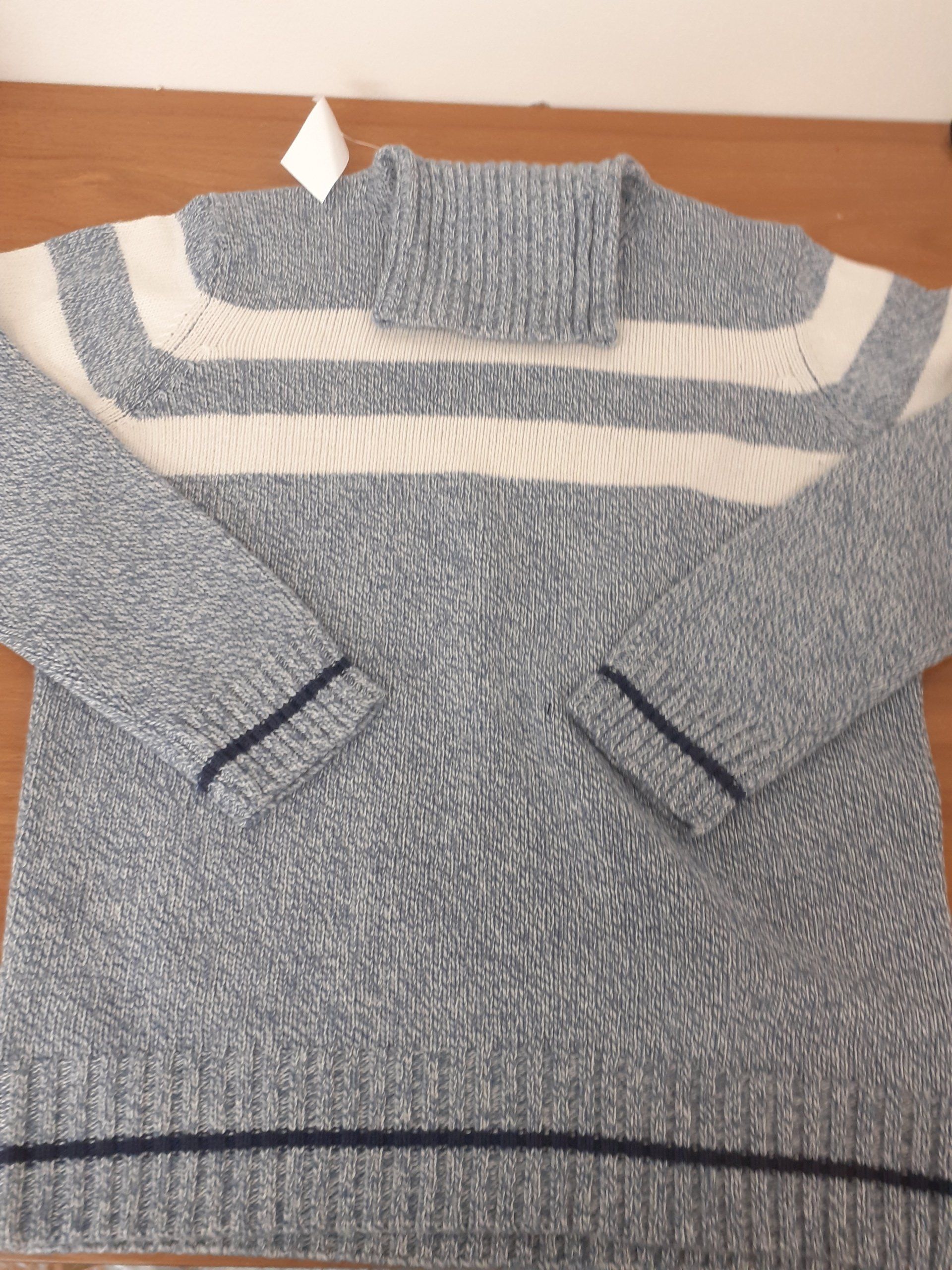 Maglione a righe grigie e bianche con collo alto, steso su un tavolo.