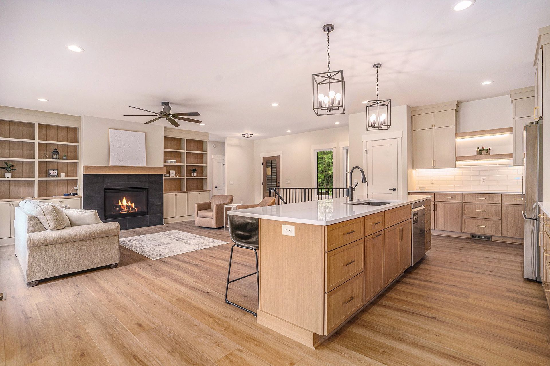 Open-concept living room and kitchen with a fireplace, light wood floors, and neutral cabinets.