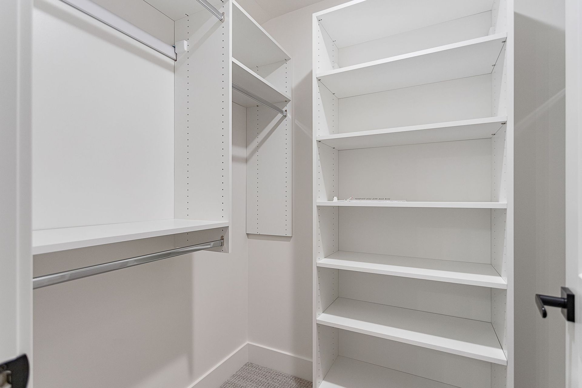 A walk-in closet featuring white wooden shelving and hanging rods on two adjacent walls, set against neutral walls.