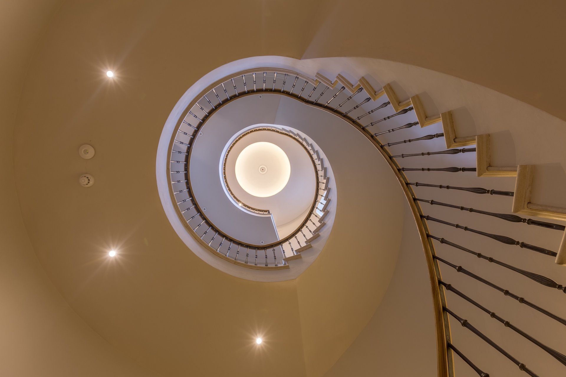 Looking up at a spiral staircase with lights on the ceiling.