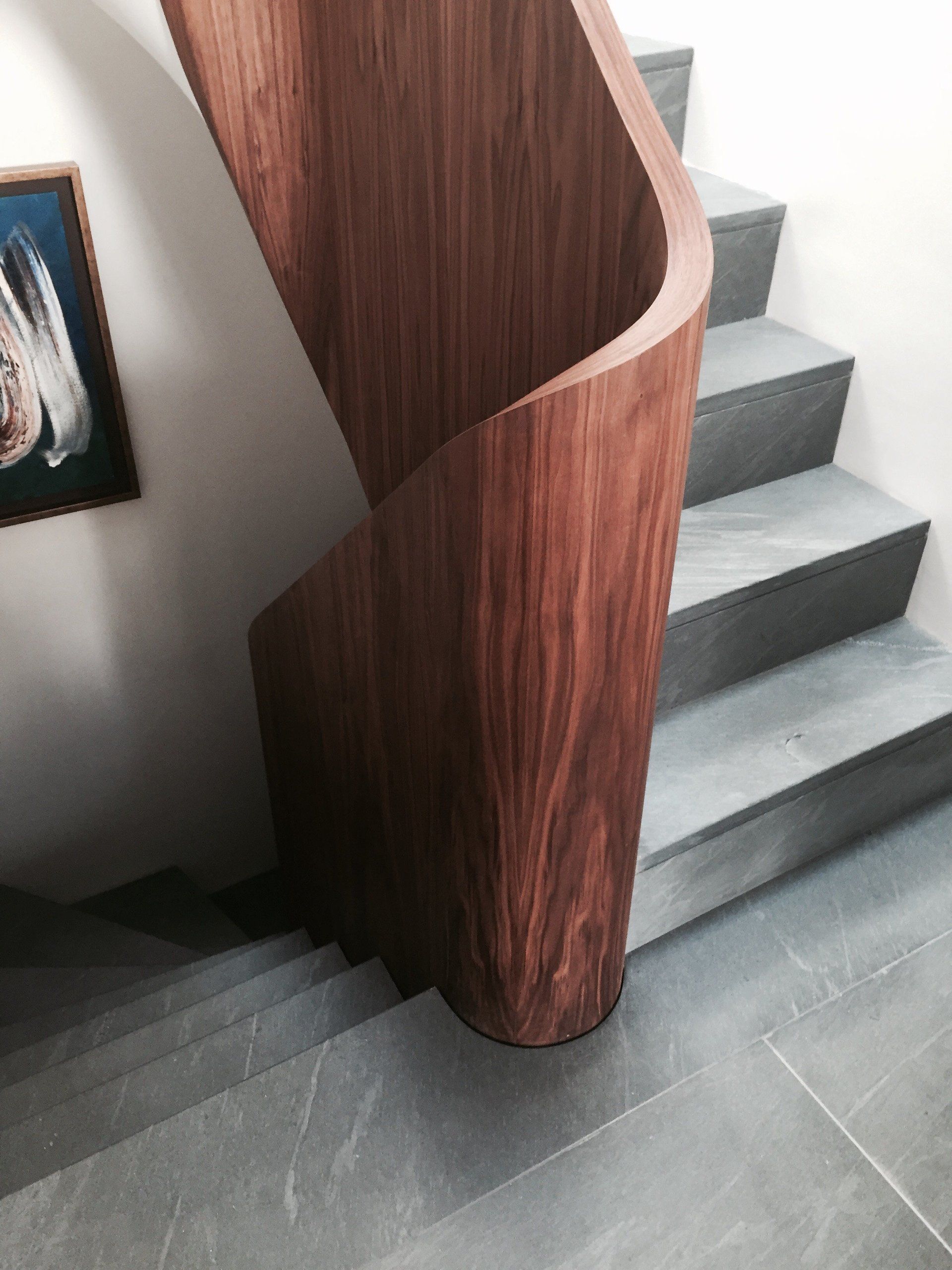 A wooden spiral staircase with a painting on the wall behind it