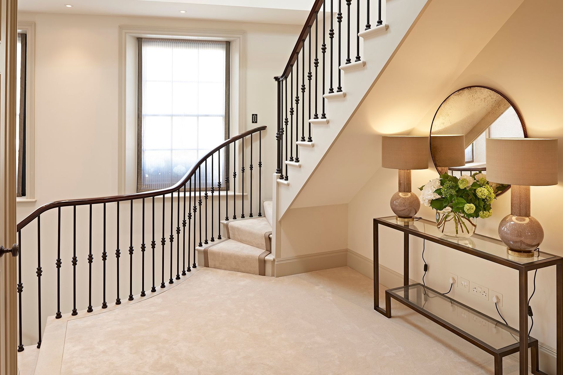 A hallway with a staircase and a table with lamps on it