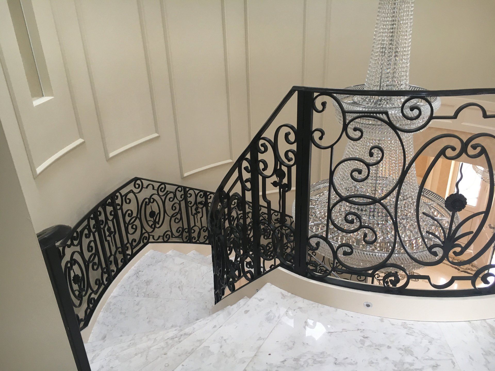 A staircase with a wrought iron railing and a chandelier hanging from the ceiling.