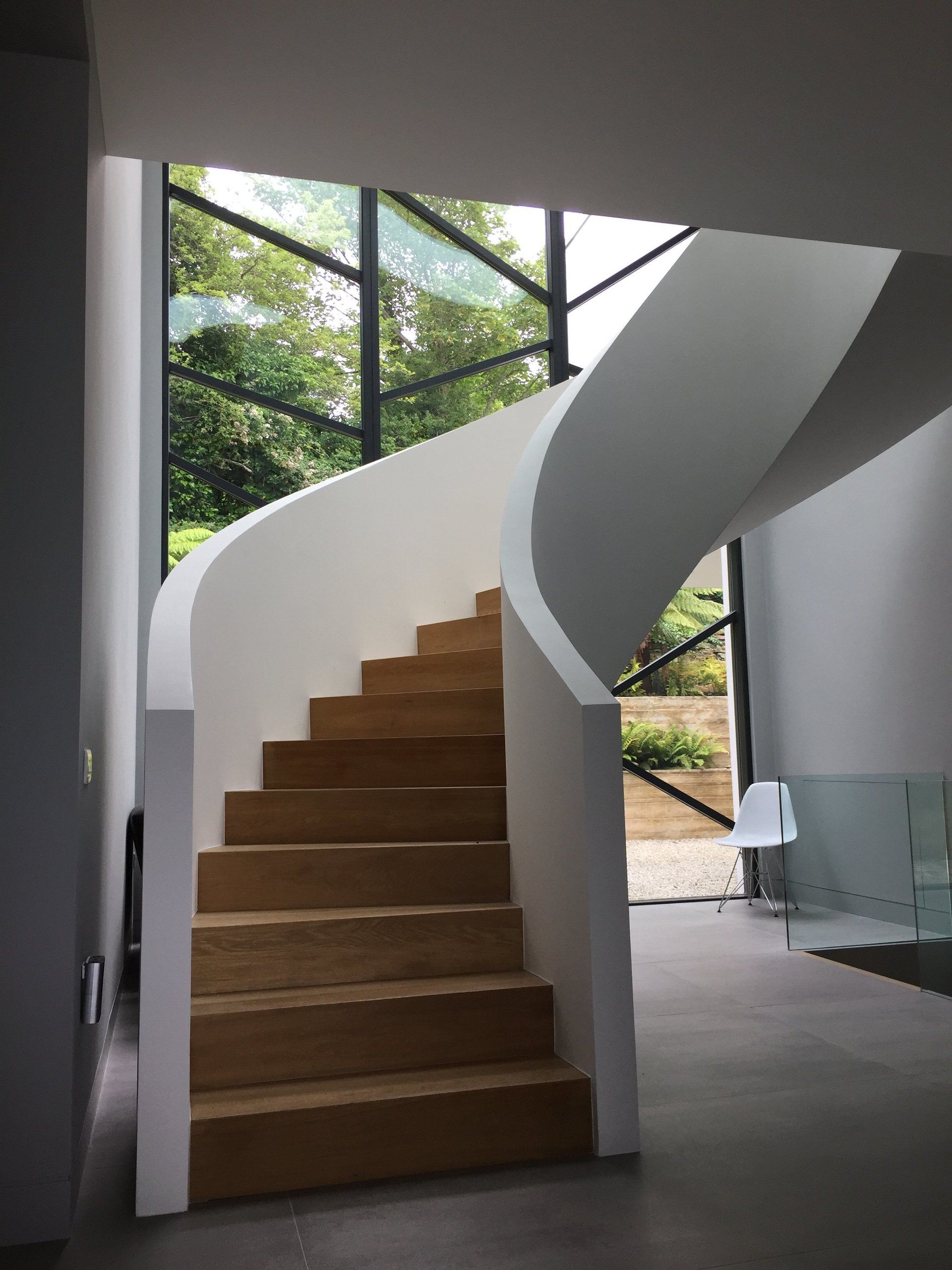 A spiral staircase in a house with wooden steps and a glass railing.