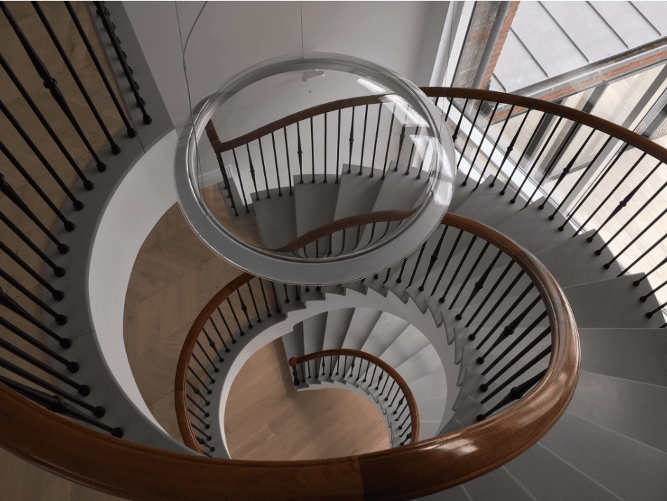 A spiral staircase with a wooden railing and a light hanging from the ceiling