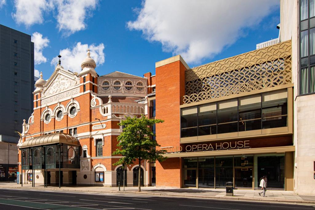 A large brick building with a lot of windows is on the side of a city street.