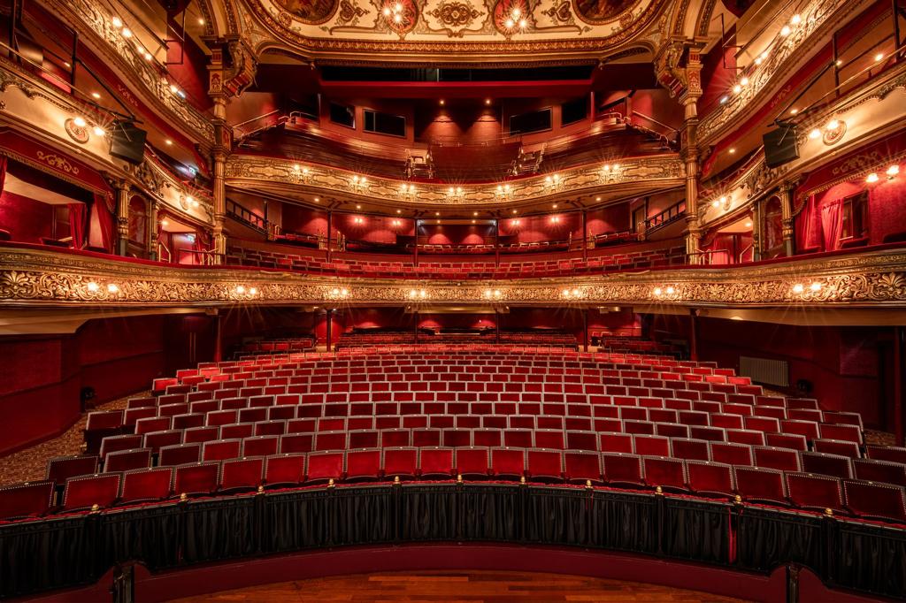 A large empty theatre with red seats and a stage.