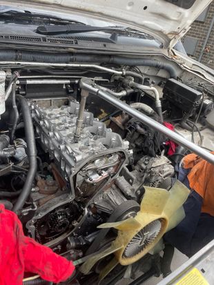 Car engine heavily damaged after a fire, covered in soot and debris.