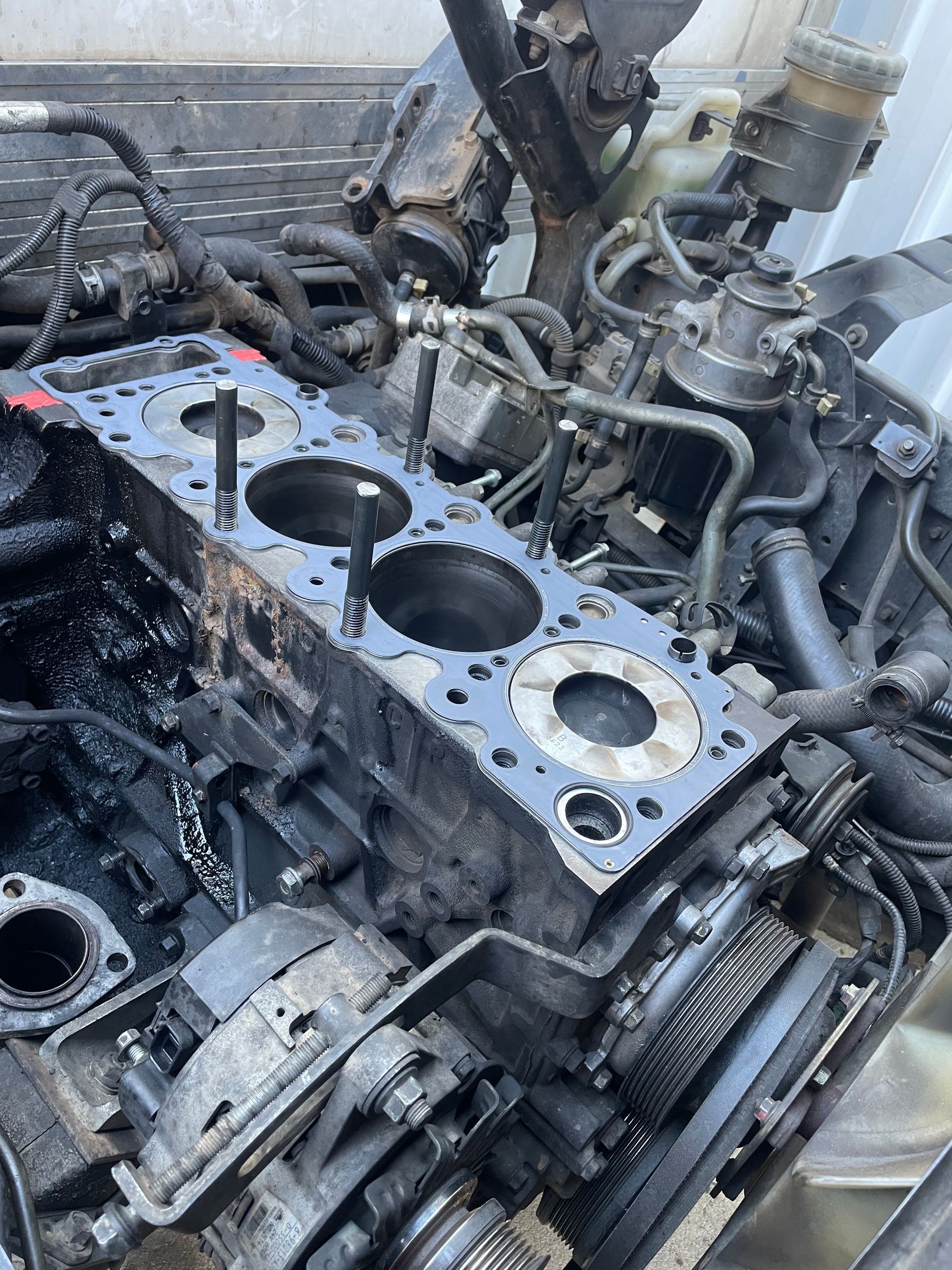 Disassembled diesel engine, black and oily, with open cylinder head and visible pistons, outdoors.