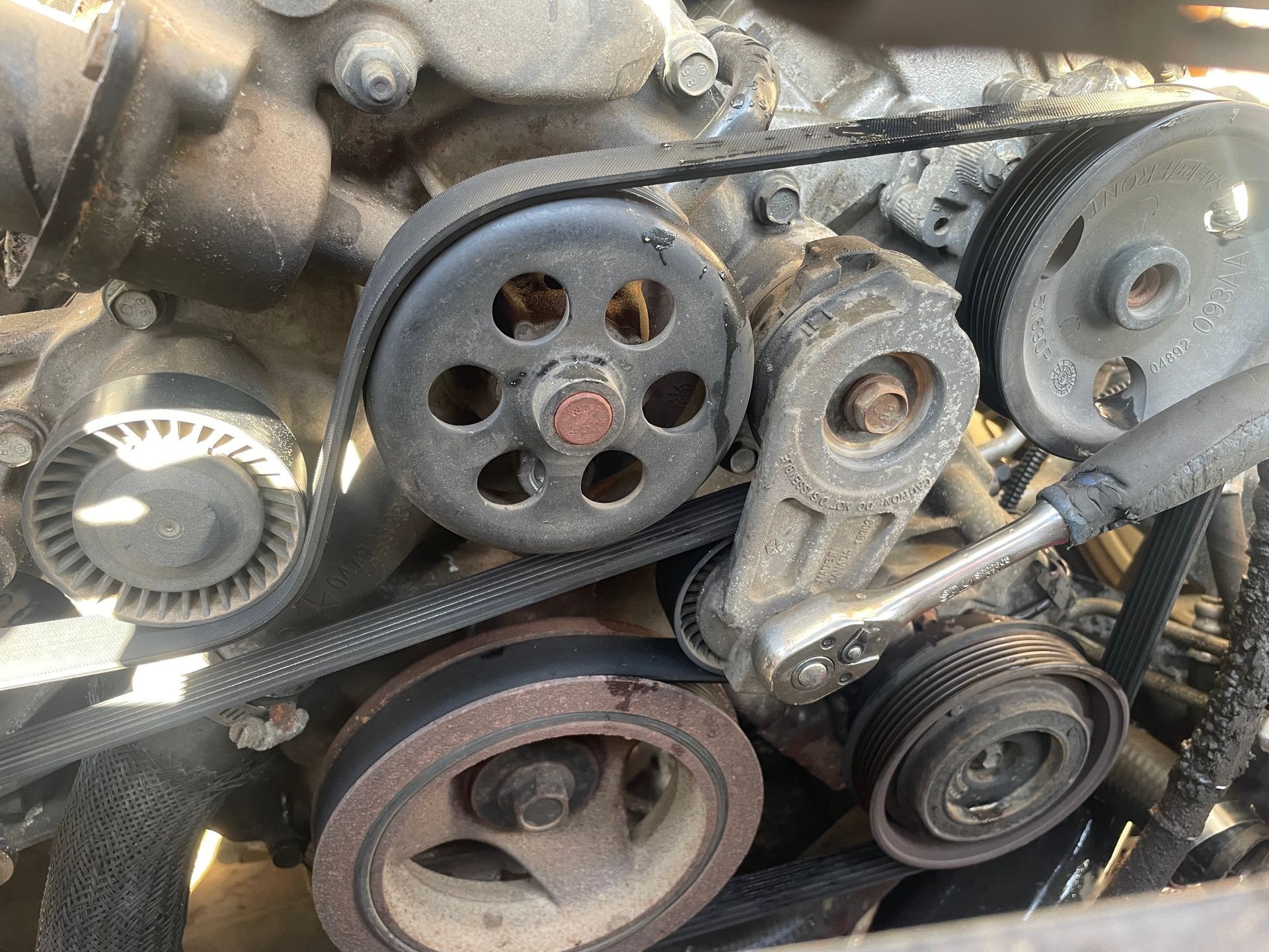 Close-up of a vehicle's engine with a serpentine belt wrapped around various pulleys and tensioner.