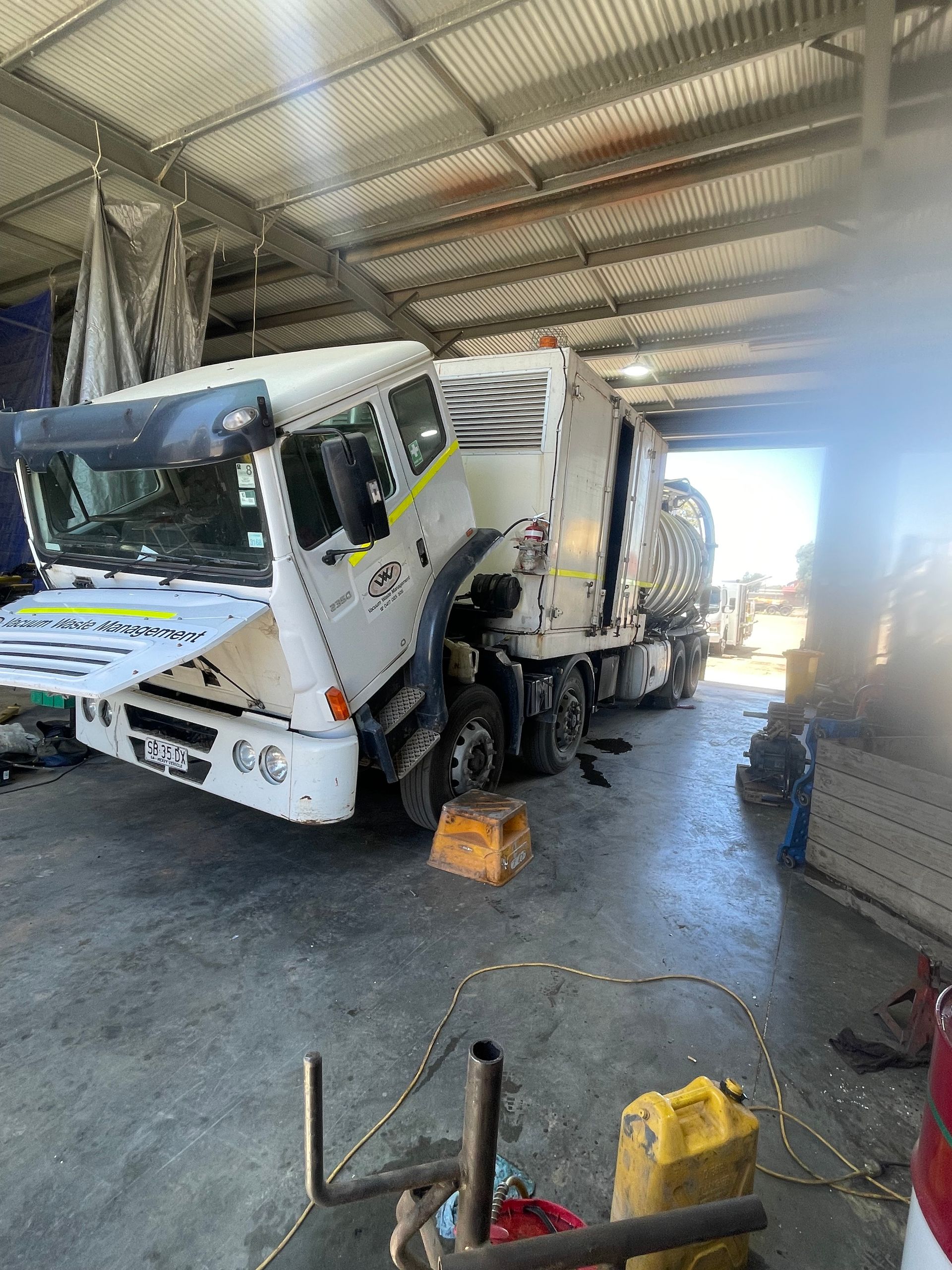 White and yellow garbage truck being worked on inside a workshop.