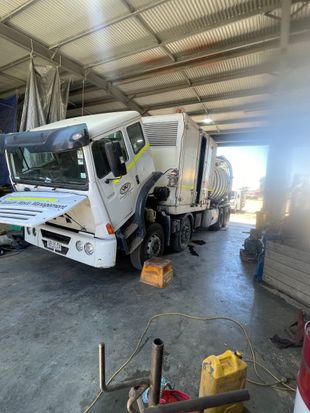 White and yellow garbage truck being worked on inside a workshop.