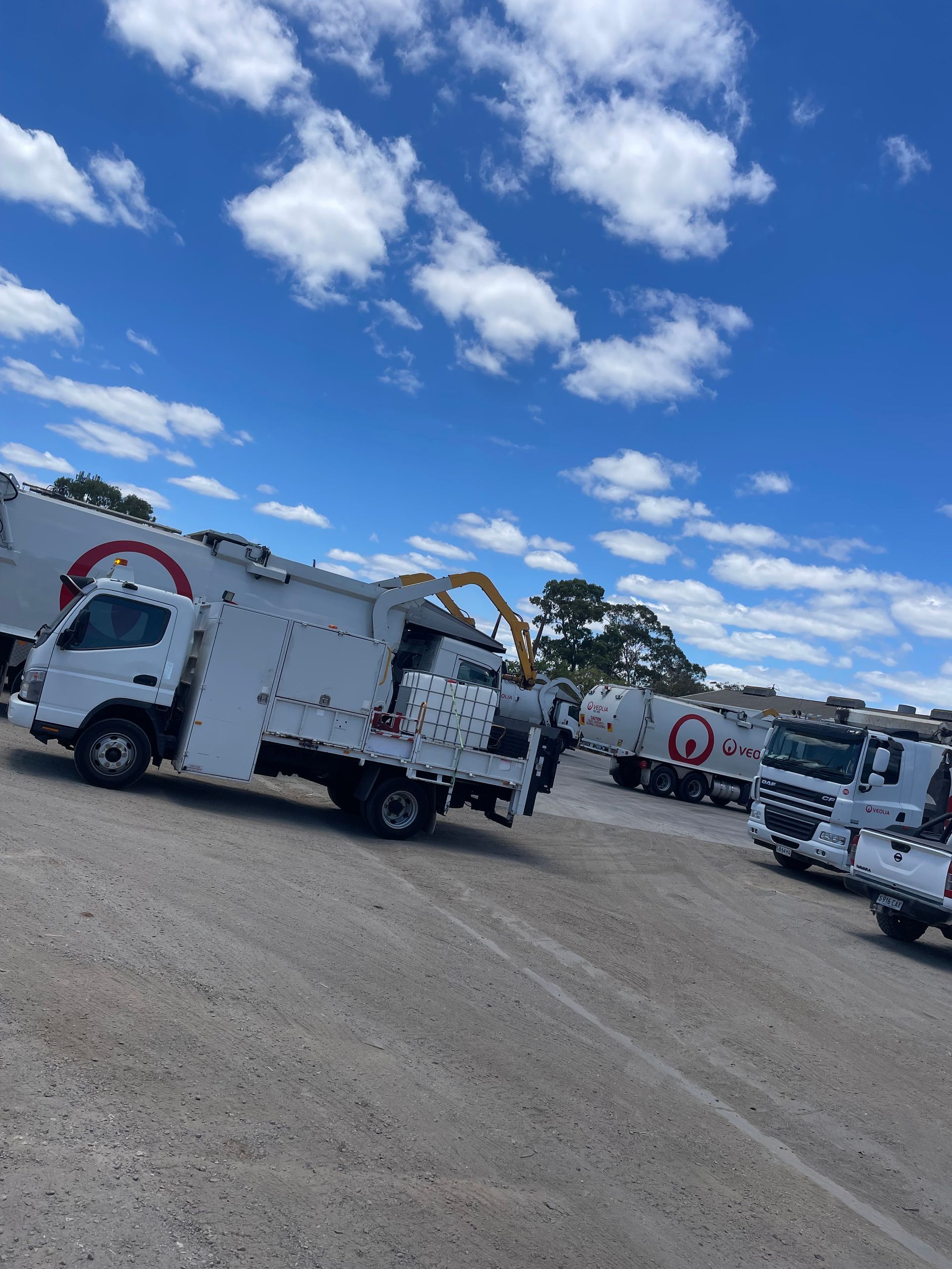 White trucks with red logos parked on gravel under a blue sky with clouds.