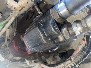Close-up of a black truck component with silver and red fittings; surrounded by tubes and wires, in an engine bay.