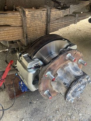 Close-up of a truck's rear axle with new brake rotor, caliper, and wheel hub partially installed.
