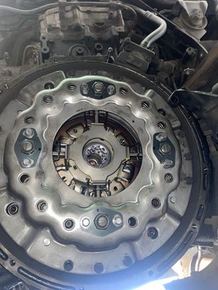 Metallic car clutch assembly; bolts, gears, and center component visible. Engine bay setting.