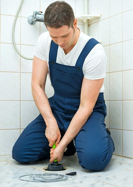 A man is kneeling down in a bathroom using a plunger.