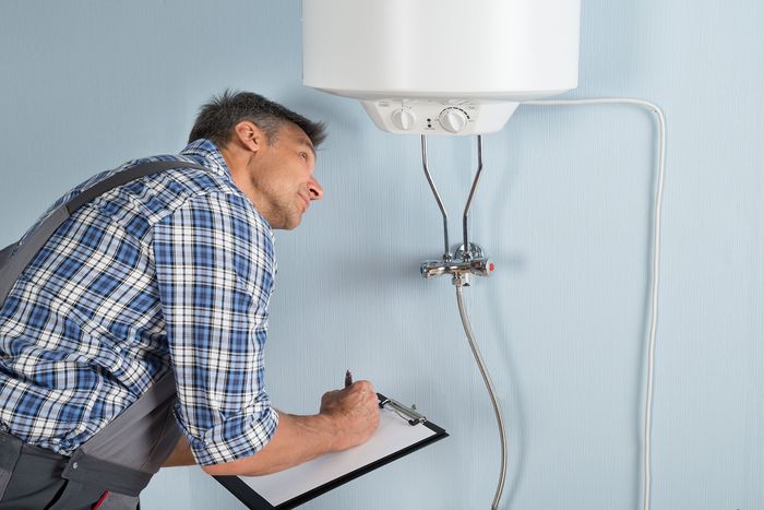 A man is writing on a clipboard next to a water heater.