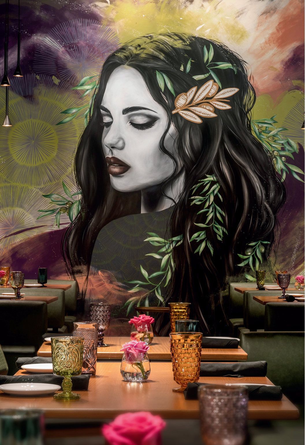 Woman's portrait mural with leafy crown, in a restaurant setting.