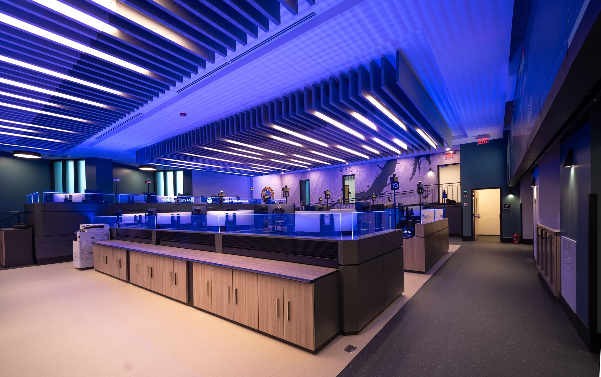 Modern office interior with blue lighting and workstations. Wooden cabinets line the floor.
