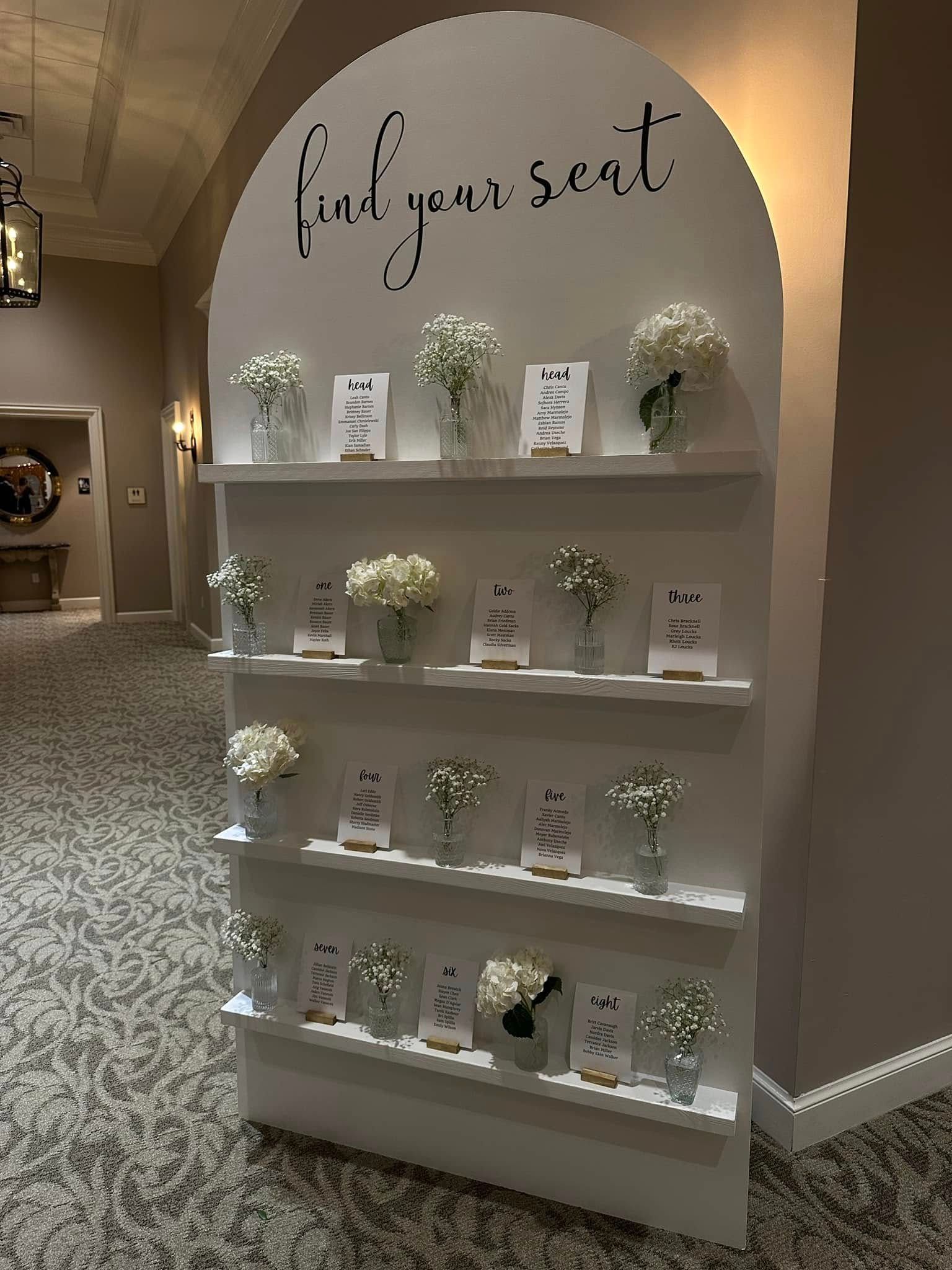 A white shelf with flowers on it and a sign that says `` find your seat ''.