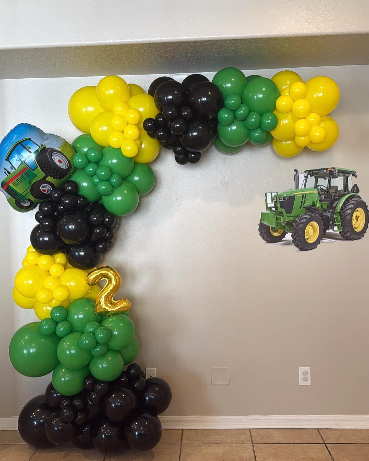 A green and yellow balloon arch with a john deere tractor on the wall.
