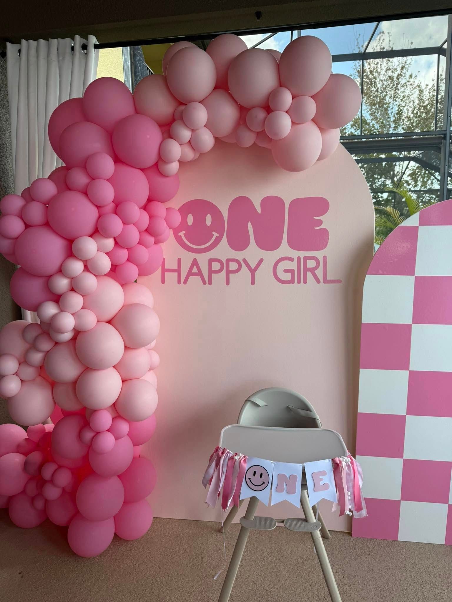 A baby chair is sitting in front of a wall decorated with pink balloons.
