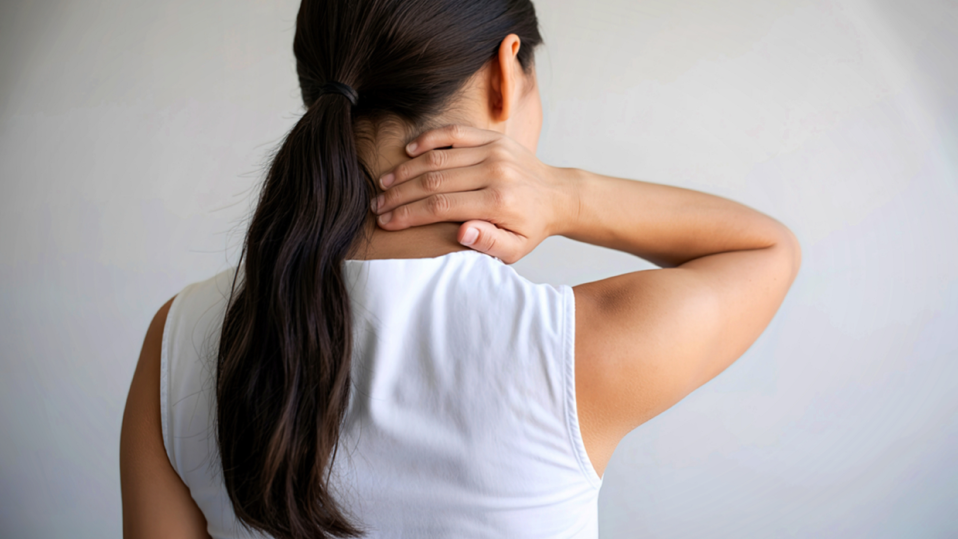 Woman holding her hand to the back of her neck, possibly experiencing pain.