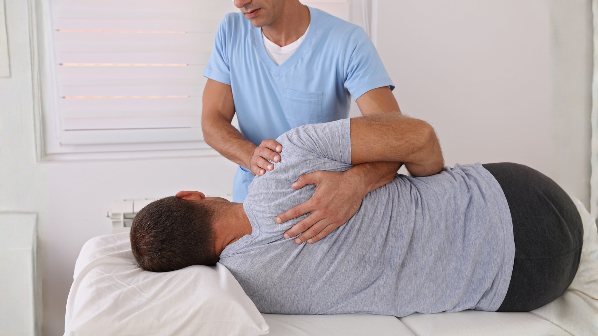 Man receiving shoulder adjustment from therapist in a clinical setting.