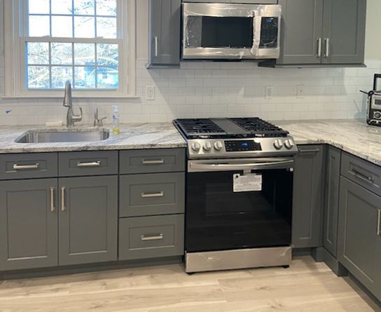 Gray kitchen with stainless steel appliances, sink, and stove. White countertops and cabinets.