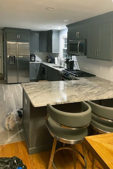 Gray kitchen with island seating. Stainless steel appliances, granite countertops, and wooden floors.