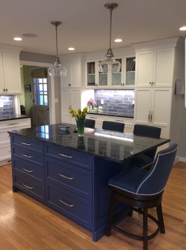 Kitchen with blue island, black countertop, white cabinets, wood floor, and two pendant lights.