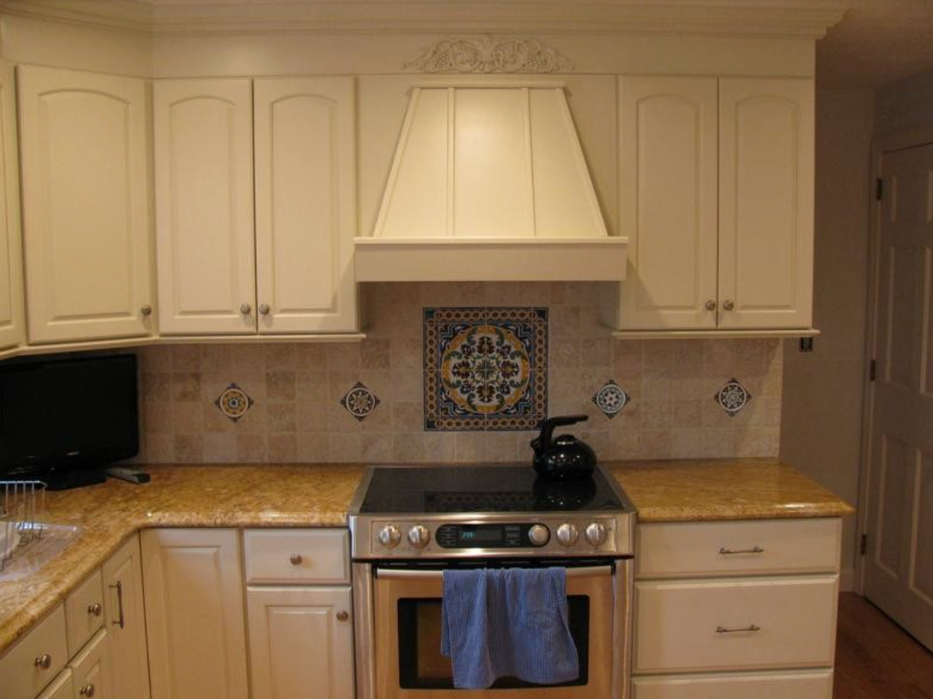 Cream-colored kitchen with cabinets, a stove, and a decorative tiled backsplash above the range.