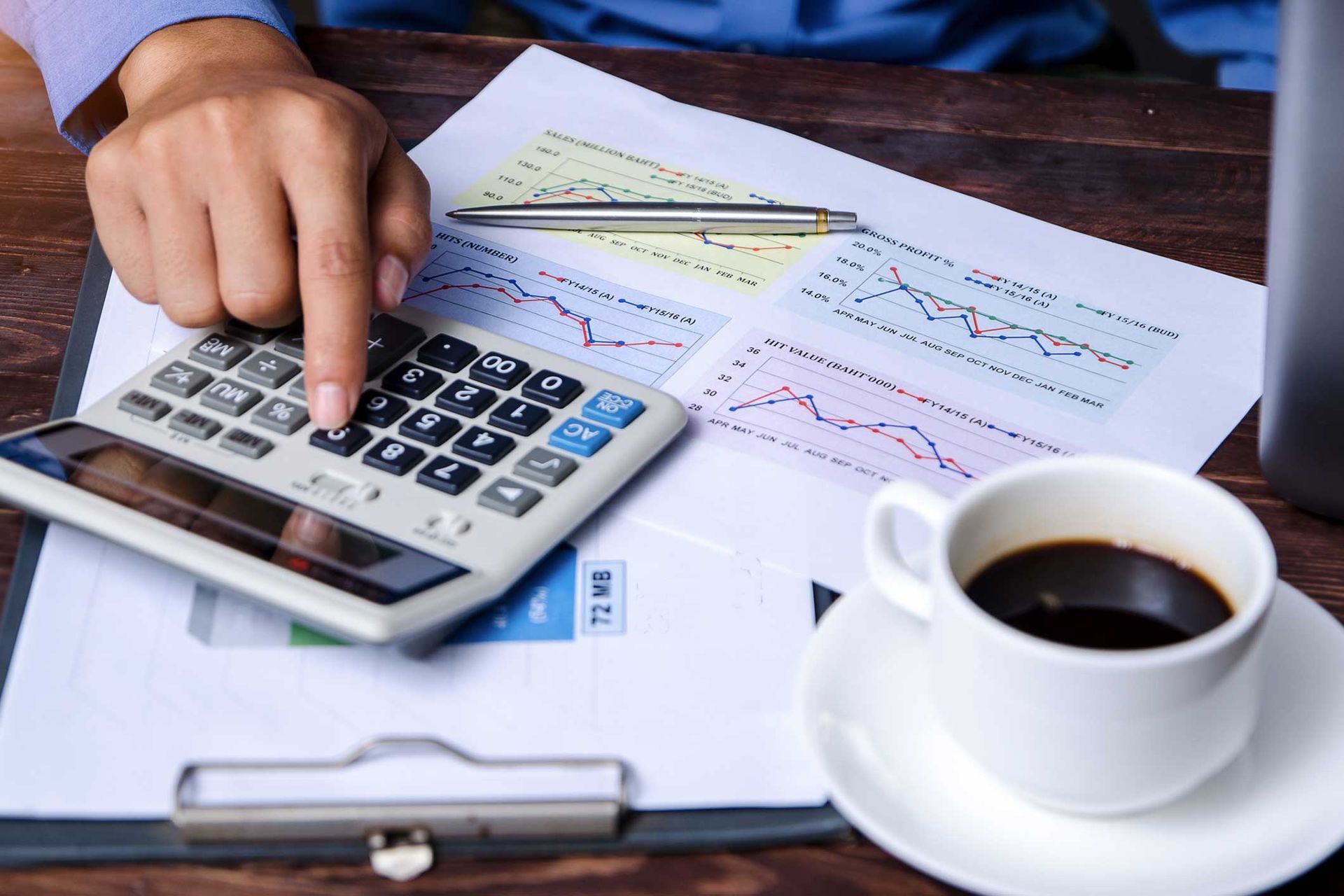 A person is using a calculator next to a cup of coffee.