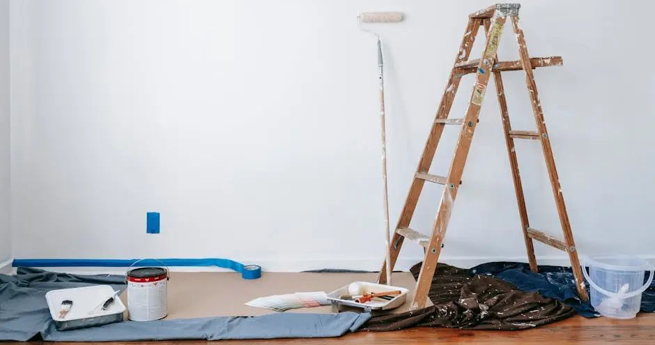 Ladder and paint supplies set up for painting a white wall.