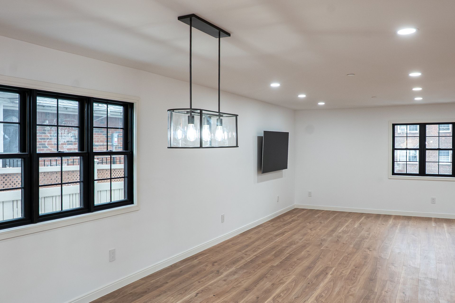 An empty living room with hardwood floors and a chandelier hanging from the ceiling