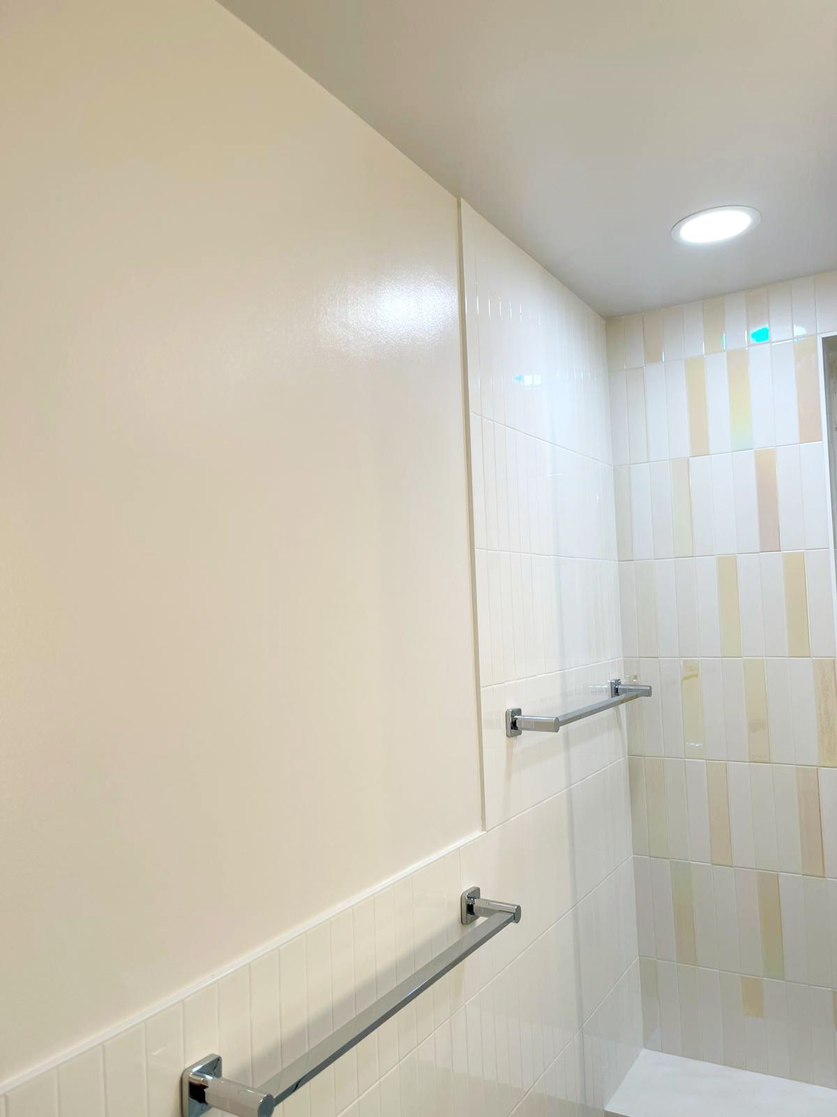 A bathroom with white tiles and a towel rack on the wall