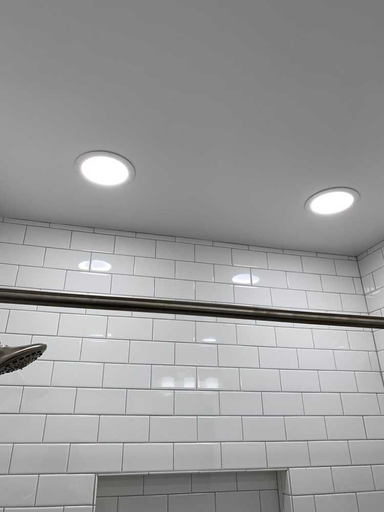 A shower head is hanging from the ceiling in a bathroom with white tiles