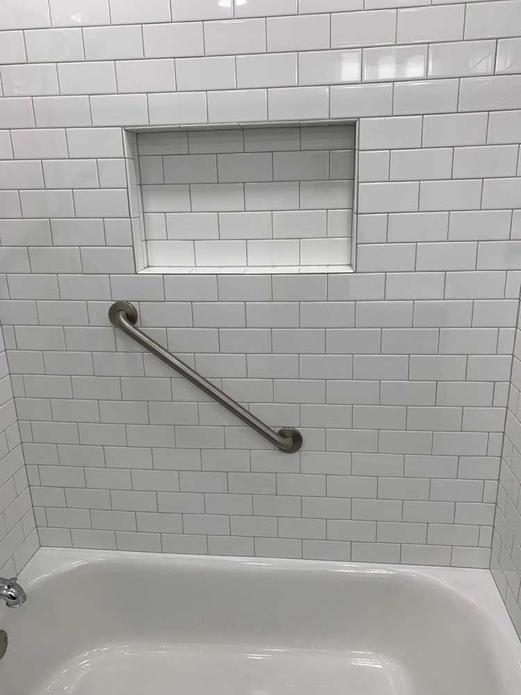 A bathtub with a stainless steel handle and a subway tile wall