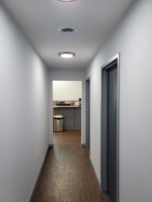 A long hallway with white walls and wooden floors leading to a kitchen