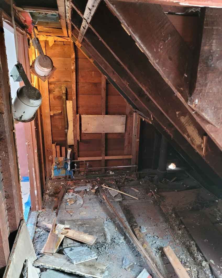 A room with a lot of junk in it and a staircase in the background